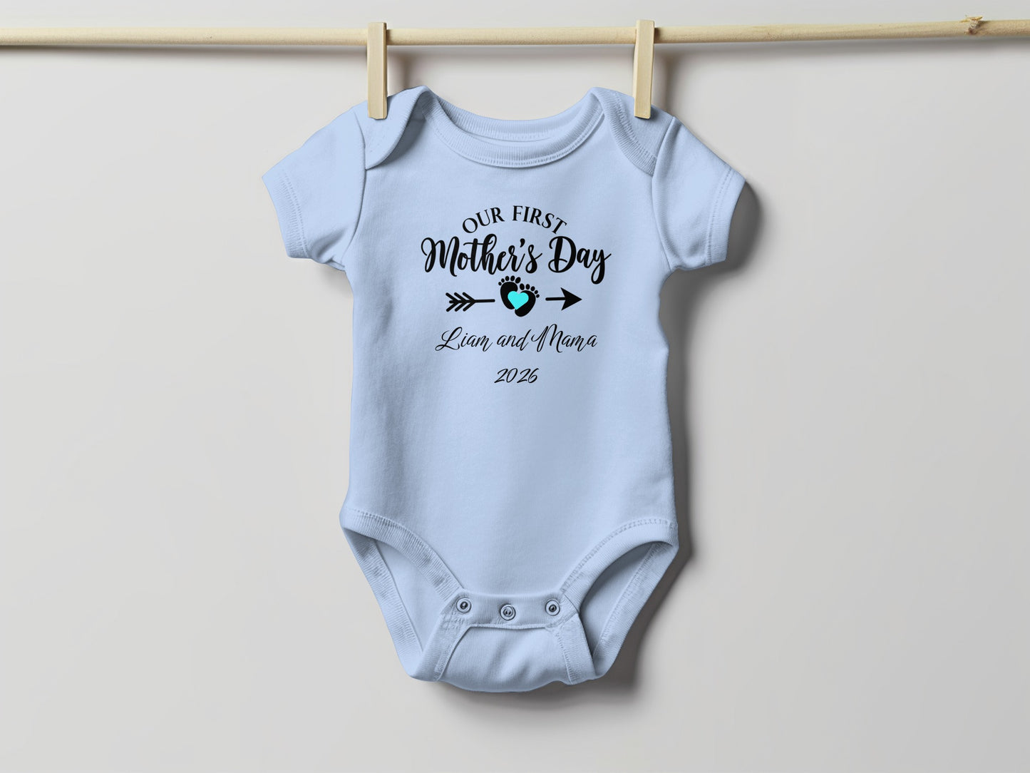 Light blue baby onesie with "Our First Mother's Day" text and date.