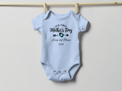 Light blue baby onesie with "Our First Mother's Day" text and date.